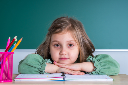 Little pretty girl sitting in the classroom at the gray desk and posing.の写真素材