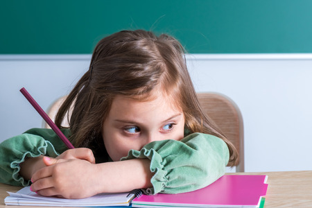 Little pretty girl sitting in the classroom at the gray desk and draws.