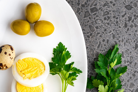 Boiled chicken eggs with quail eggs, olive and parsley on the white plate, healthy foodの写真素材