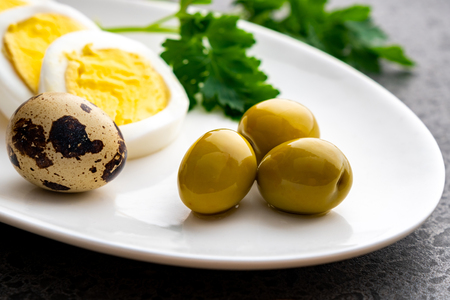 Boiled chicken eggs with quail eggs, olive and parsley on the white plate, healthy foodの写真素材