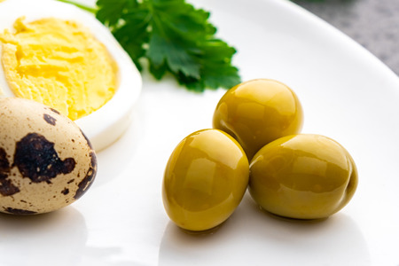 Boiled chicken eggs with quail eggs, olive and parsley on the white plate, healthy foodの写真素材