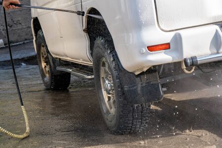 Shot of a man washing his car under high pressure water outdoors. Industry.