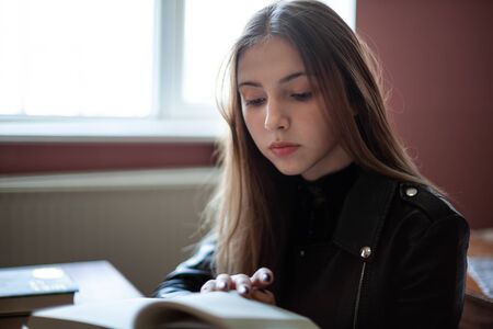 Beautiful teenager schoolgirl sitting in the library and reading a book, educationの写真素材