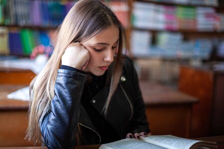 Beautiful teenager schoolgirl sitting in the library and reading a book, education