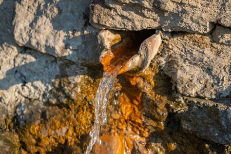 Close up view of a water fountain. Water coming from a hole on the wall covered with algae. Georgia.の写真素材