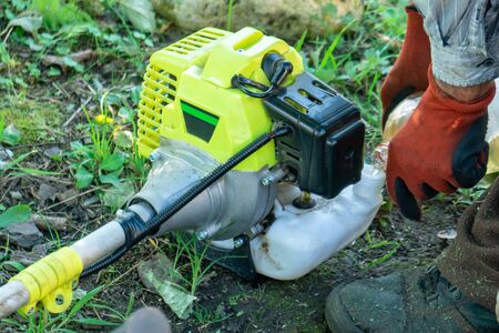 Farmer adding petrol gas to the gasoline tank of the trimmer brushcutter in the field. Technology.の写真素材