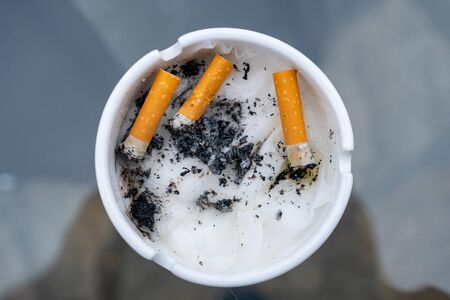 White dirty ashtray with cigarette stubs. Cigarette butts