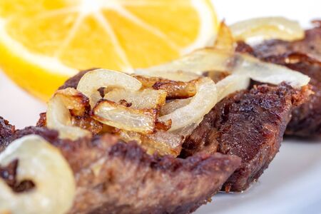 Roast beef with onion and lemon on a white plate. Food.