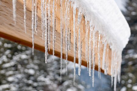 Icicles hang from the snowy roof of a mountain cottage, winter.