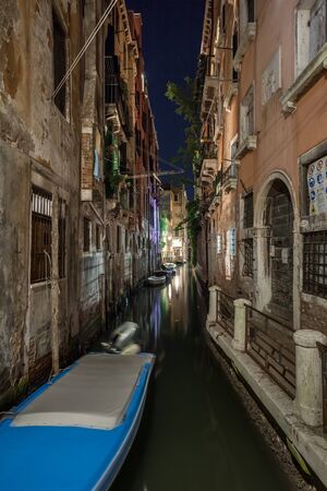 Narrow canal with boats and vintage houses at dusk. Venice city at night, Italy. Traditional Venice street in twilight.の写真素材