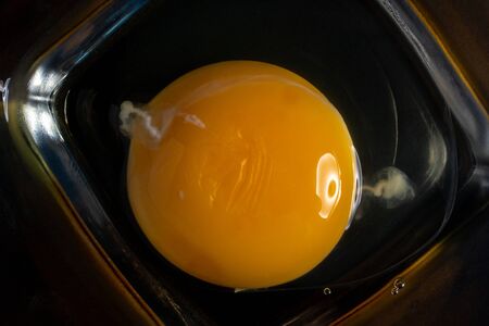 Top view of broken eggs yolk in a glass bowl isolated on a black background