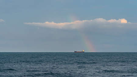 Tankers on sea horizon and short wide rainbows, clouds in sky. Landscapeの写真素材