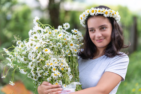 Cute teenage girl with a wreath of daisies on her head and a bouquet of daisies in her hands. Portraitの写真素材