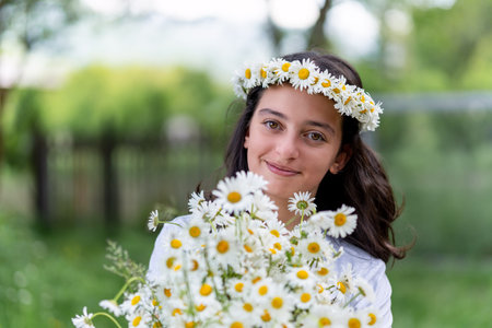 Cute teenage girl with a wreath of daisies on her head and a bouquet of daisies in her hands. Portraitの写真素材