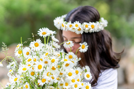 Cute teenage girl with a wreath of daisies on her head and a bouquet of daisies in her hands. Portraitの写真素材