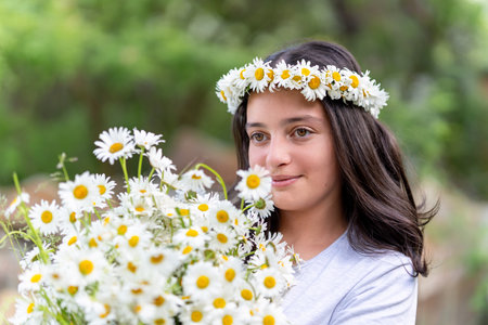 Cute teenage girl with a wreath of daisies on her head and a bouquet of daisies in her hands. Portraitの写真素材