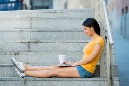 attractive latin woman in her twenties happy and working on her laptop outside in europe. の写真素材
