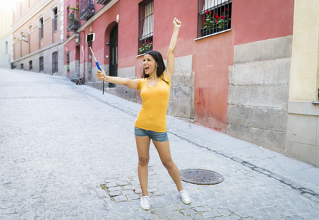young attractive and sweet latin woman smiling happy taking self portrait selfie photo with mobile phone camera outdoors at urban city background in blogger conceptの写真素材