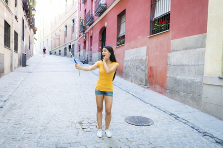 young attractive and sweet latin woman smiling happy taking self portrait selfie photo with mobile phone camera outdoors at urban city background in blogger conceptの写真素材