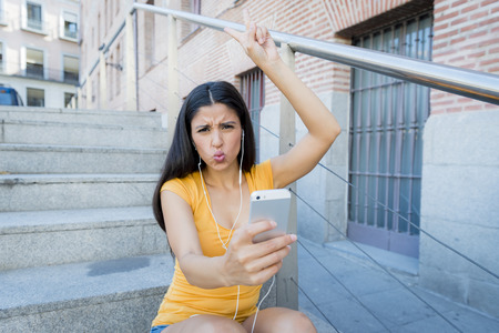 attractive latin woman in her twenties happy listening to music on her mobile smart phone while drinking a coffee sitting on stairs. の写真素材