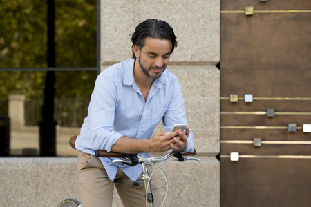 young happy attractive hispanic man in casual trendy clothes smiling cheerful using mobile phone on vintage cool retro bicycle in modern stylish lifestyle urban style concept の写真素材