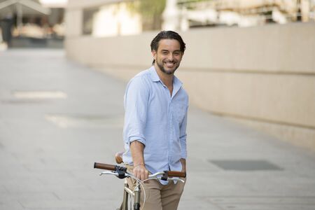 young happy attractive latin man in casual trendy clothes smiling cheerful riding on vintage cool retro bicycle in modern stylish lifestyle urban style concept の写真素材