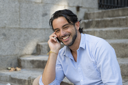 young attractive latin man on city staircase talking happy on mobile phone looking satisfied and confident in communication technology and lifestyle business success conceptの写真素材