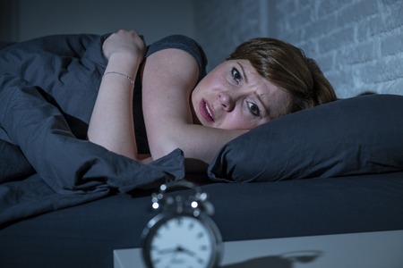 Young attractive red haired caucasian woman lying in bed late at night trying to sleep suffering from insomnia, nightmares or sleeping disorders. looking stressed and exhausted.の写真素材