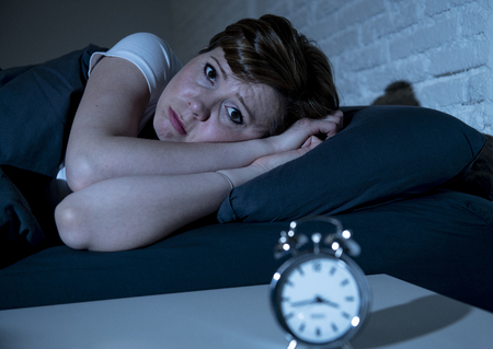 Young attractive red haired caucasian woman lying in bed late at night trying to sleep suffering from insomnia, nightmares or sleeping disorders. looking stressed and exhausted.の写真素材