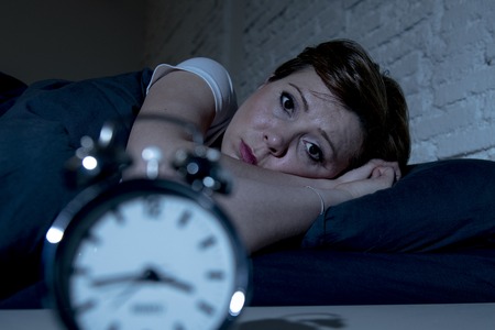 Young attractive red haired caucasian woman lying in bed late at night trying to sleep suffering from insomnia, nightmares or sleeping disorders. looking stressed and exhausted.の写真素材