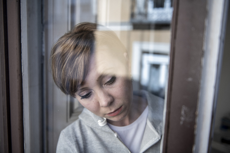 young beautiful depressed unhappy caucasian woman looking worried and sad through the window at home. feeling worthless and in pain. closeup. Depression and crisis conceptの写真素材