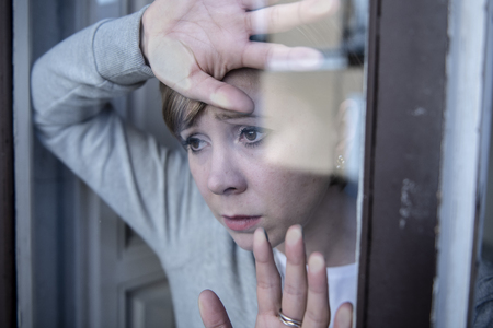 young beautiful depressed unhappy caucasian woman looking worried and sad through the window at home. feeling worthless and in pain. closeup. Depression and crisis conceptの写真素材