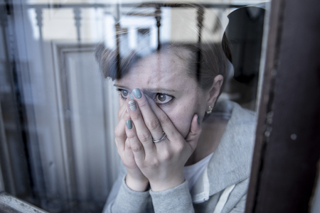 young beautiful depressed unhappy caucasian woman looking worried and sad through the window at home. feeling worthless and in pain. closeup. Depression and crisis conceptの写真素材