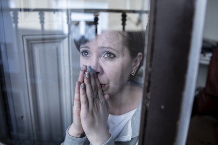 young beautiful depressed unhappy caucasian woman looking worried and sad through the window at...