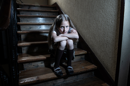 Sad, depressed, unhappy schoolgirl suffering from bullying and abuse feeling lonely and hopeless sitting on stairs with dark light. School isolation, bullying, harassment and abuse conceptの写真素材