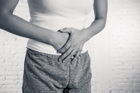 Close up of a young woman having painful stomachache holding hands on her belly. Body pain, gastritis, constipation, period pain and menstrual cramps. Female health conceptの写真素材