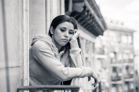 Attractive latin depressed lonely woman staring out feeling sad, pain, grief on a balcony at home. Crisis, depression and mental health conceptの写真素材