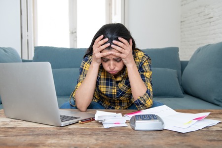 Young attractive woman worried at home banking and accounting home and credit card expenses with computer laptop doing paperwork in living cost stress and paying bills problemの写真素材