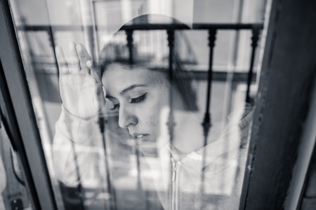 Young beautiful depressed unhappy latin woman looking worried and sad through the window at home. feeling worthless and in pain. closeup. Depression and crisis conceptの写真素材