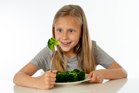 happy young blonde girl with thumbs up enjoying and loving eating her broccoli vegetables on a plate with knife and fork in healthy children eating conceptの写真素材