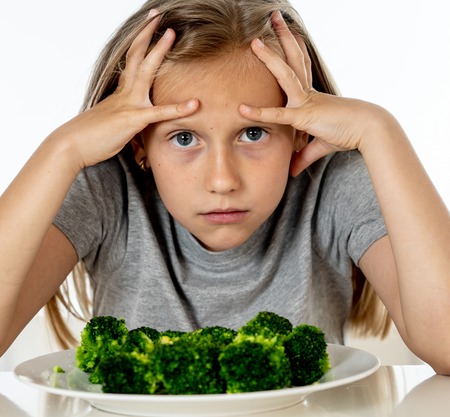 Nutrition & healthy eating habits for kids healthy eating concept. Children do not like to eat vegetables. Little cute kid girl refuse to eat healthy broccoli vegetables on a white backgroundの写真素材