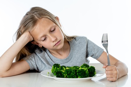 Nutrition & healthy eating habits for kids healthy eating concept. Children do not like to eat vegetables. Little cute kid girl refuse to eat healthy broccoli vegetables on a white backgroundの写真素材