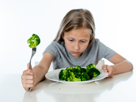 Nutrition & healthy eating habits for kids healthy eating concept. Children do not like to eat vegetables. Little cute kid girl refuse to eat healthy broccoli vegetables on a white backgroundの写真素材