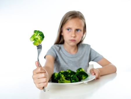 Nutrition & healthy eating habits for kids healthy eating concept. Children do not like to eat vegetables. Little cute kid girl refuse to eat healthy broccoli vegetables on a white backgroundの写真素材