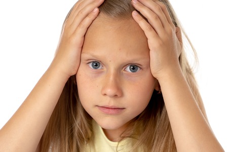 sweet young little schoolgirl pulling her hair desperate in stress while sitting on school desk doing homework tired and exhausted screaming crazy isolated on white background in education conceptの写真素材