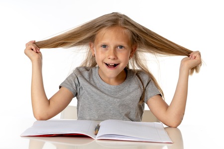 sweet young little schoolgirl pulling her hair desperate in stress while sitting on school desk doing homework tired and exhausted screaming crazy isolated on white background in education conceptの写真素材