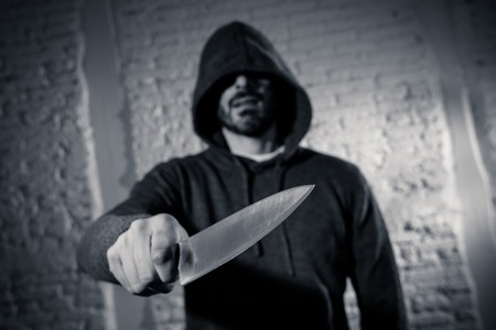 close up of a hands holding a knife of dangerous hooded man standing in the dark in London knife crime concept.の写真素材