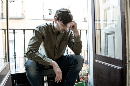 Lonely young man looking outside house balcony looking depressed, destroyed, sad and suffering emotional crisis and grief thinking of taking a difficult and important life decisionの写真素材