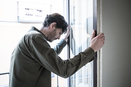 Lonely young man looking outside house balcony looking depressed, destroyed, sad and suffering emotional crisis and grief thinking of taking a difficult and important life decisionの写真素材