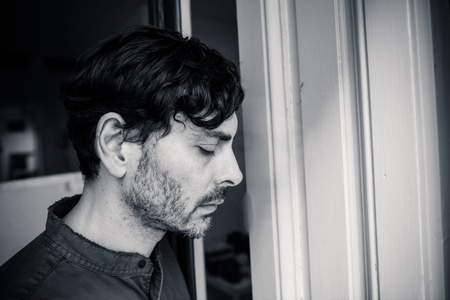 Lonely young man looking outside house balcony looking depressed, destroyed, sad and suffering emotional crisis and grief thinking of taking a difficult and important life decisionの写真素材